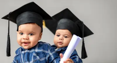 Two cute babies, one is holding a college degree and both have graduation caps on.