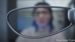A closeup view looking through one lens of a pair of glasses. The image is blurred through the lens but you can tell that it is a person facing the camera. Overlayed on the lens is green colored text that is too small to read.