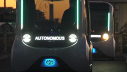 Two small, white, boxy autonomous vehicles shown at night