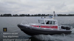 A red and white rescue ship that is about 25 feet long is moving on a large body of water. The sky is overcast and a shoreline of trees can be seen on the horizon.