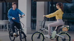Two people are sitting on eBikes facing each other. One bike is light colored the other is dark.