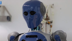 A closeup view of the head and shoulders of a dark blue and gray humanoid robot. The head of the robot has two cutouts for the eyes.