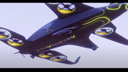 A closeup view from below of a navy blue and yellow aircraft in the air. It has wings in front and back that have cutouts for drone propellers, 2 on each section of the wings. There is also a small propeller on the front as you might see on any prop plane. 