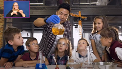 a group of 10-12 year old students watching an instructor holding a chemistry flask with gold liquid