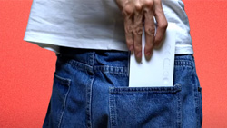 A closeup view of the back of a person wearing jeans and a white tshirt putting a thin white rectagular device in their right back pocket