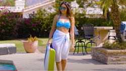 A person in a bathing suit is walking by the pool carrying a small suitcase sized white and avocado-green plastic robot.