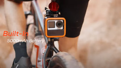 A closeup of a small, safety-orange trimmed, square, camera placed just below the reflector on a bike.