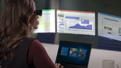 a woman wearing smart glasses working on a laptop with 3 holographic images above the computer