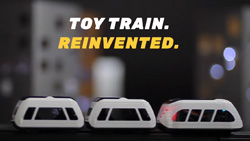 Three black and white toy train cars are sittng on toy tracks. The text reads Toy Train. Reinvented.