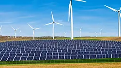 An array of solar panels is in the foreground and wind turbines in the background