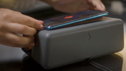 A closeup of person placing their phone on a grey box about the size of a brick