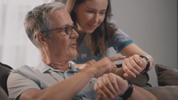 A front view of a person holding their wrist up to show another person behind them their watch. The person behind is wearing a similar watch