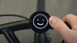 A closeup of a round black device mounted in the middle of a bike's handlebars. There is a white smiley face on the display.