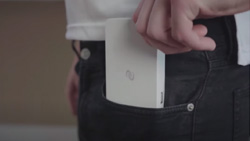 A closeup of a person putting a small white rectangular device in their jean's pocket.