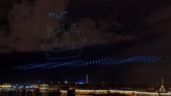 A wide view of the night shy over a city shows a representation of a sail ship, water and a bird using drones