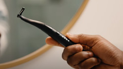 a closeup of a person holding black device that resembles a micro-shaver. It is curved at the flossing end like a toothbrush