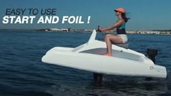 A side view of a person in a small white water craft in the water moving at high speed. The bottom of the boat is not touching the water. Two black blades are attached to the bottom of the boat and disappear into the water where presumably the waterjets are located to propel the craft.