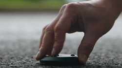 A closeup of a person placing a small black disk shaped object on pavement