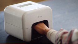 A closeup of a rounded white box with an opening in front. A person has their left hand in the machine up to the last knuckle.