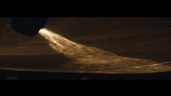 A view at night of an aircraft with no lights taking off from a runway. The exhaust is lit up leaving a trail.