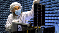 A closeup of a person in white clean room headcap, mask and full-body cover examining a small array of solar panels
