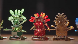 A closeup of 3 small robot figures made of circuit boards and leds. The left is light green, the middle is red, the right one is tan. 