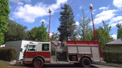 A fire truck has two tall antenna towers extended from the top of the vehicle. A white dome sits atop both antennas.