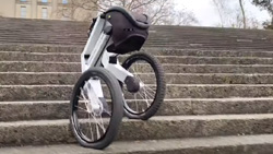 A view from the bottom of concrete steps outside shows a two-wheeled robot coming down at an ablge from left to right. The left wheel is on one step and the right wheel on the the next lower step.