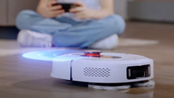 A closeup view of round, white robot vacuum on the floor in front of a child. Overlayed is blue light emitting form the robot in the front to simulate obstacle avoidance scanning.