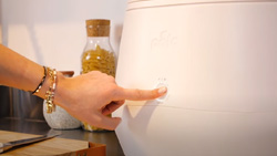 a person is pushing a button on an all white countertop machine about the size and shape of a large airfryer 