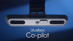 A closeup of a oblong silver device mounted on a windshield. The text reads Bluebox Co-pilot