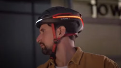 A closeup view from the side of a person wearing a black bike helmet at night with an amber LED light strip in back and a white LED strip in the front.