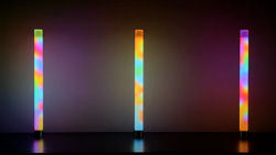 Three lighted lamps stand side by side. They are transparent tubes with a rainbow of blended colors