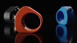 a closeup of three smart rings, red, blue and black. The material looks like plastic, it's thick, and has a black push-button and a LED on top