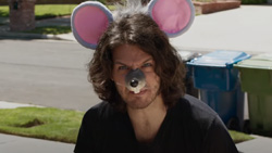 A closeup of a person in a driveway wearing mouse ears and nose looking at the camera