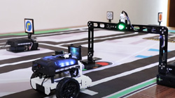 A 3-wheeled robot car is on a road track mat with signs and stop lights.